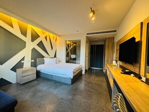 Habitació d'hotel moderna amb un llit gran, una taula de treball de fusta, un televisió de pantalla plana i un disseny de paret geomètric únic.