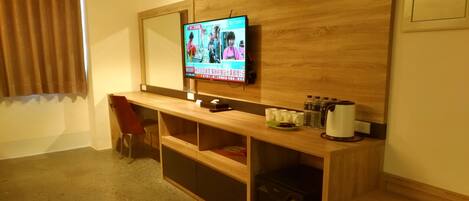 A hotel room with a wooden desk, a television mounted on the wall, a red chair, and a small cabinet.