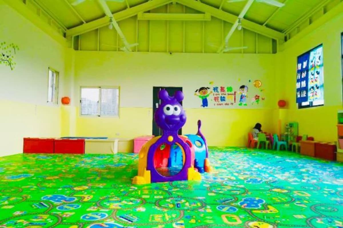 A brightly colored indoor play area with a green floor, a purple play structure, and educational posters on the walls.