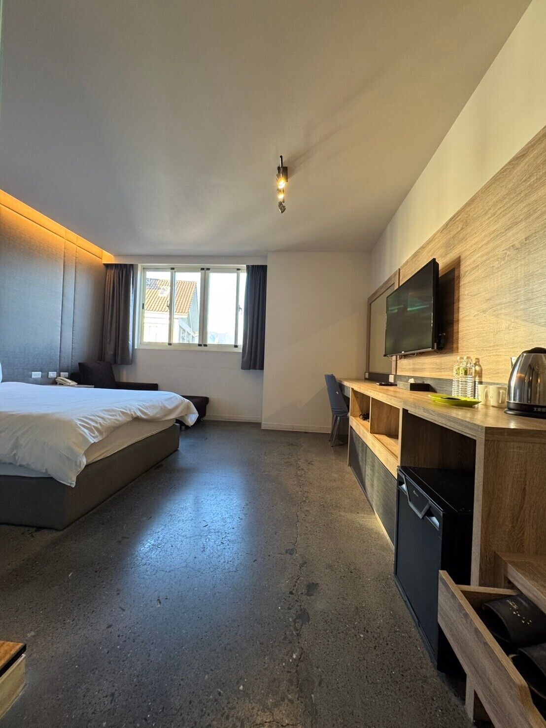A modern hotel room with a bed, a desk, a television, and a window with curtains.