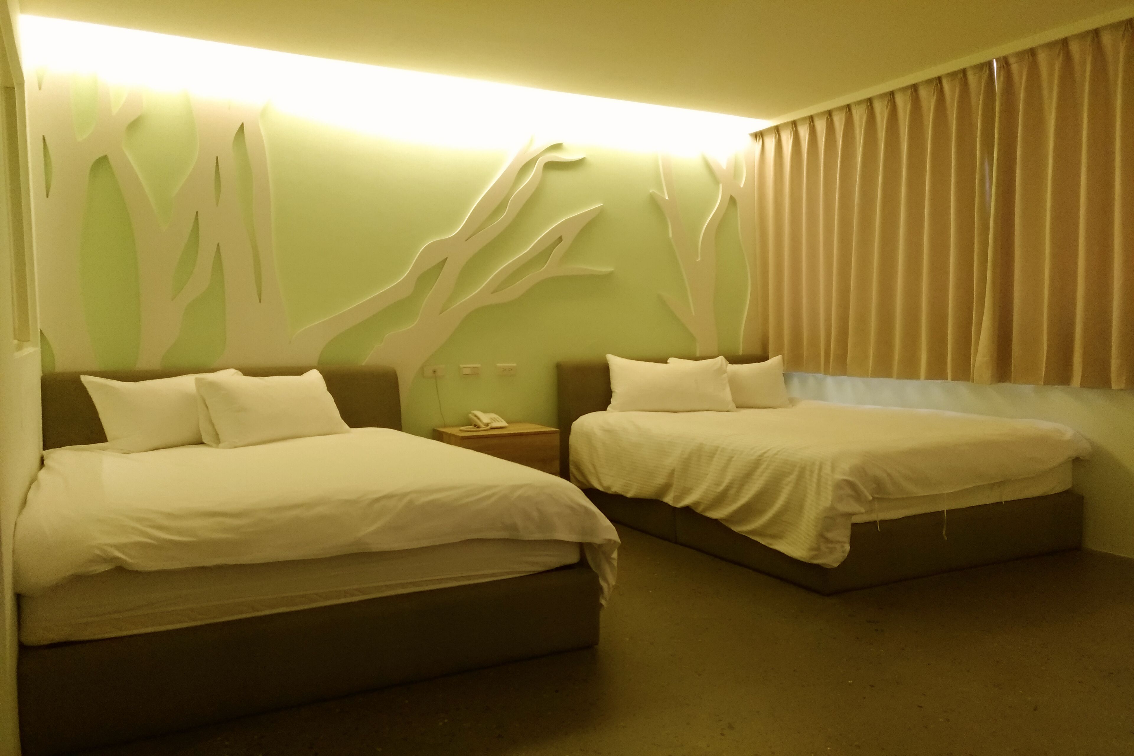 A hotel room with two beds, a nightstand, and a wall with a tree design.