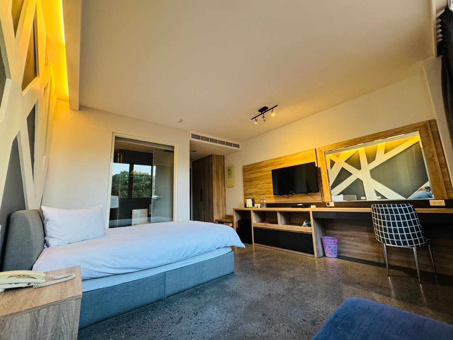 A modern hotel room with a bed, a desk, a TV, and a window.