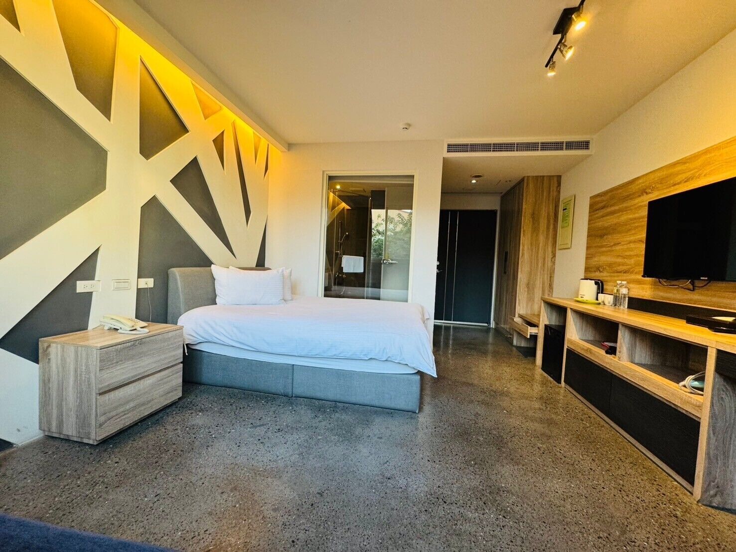 Una habitación de hotel moderna con una cama grande, una mesita de noche, un televisor y una zona de ducha.