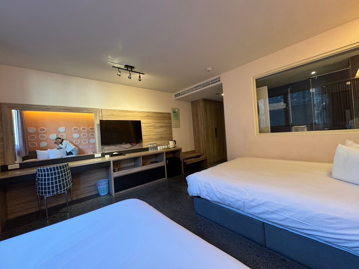 A hotel room with two beds, a TV, a desk with a computer, and a large window.