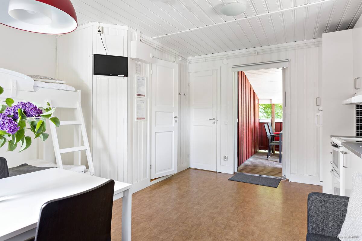 A modern kitchen with white cabinetry, a dining area with a table and chairs, and a view into a dining room with a red-striped partition.