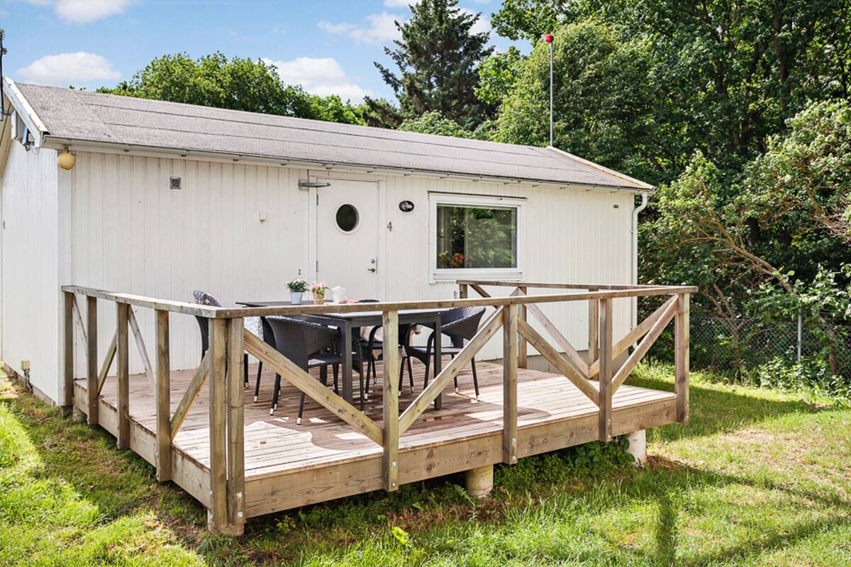 A small white cabin with a wooden deck and outdoor seating area.