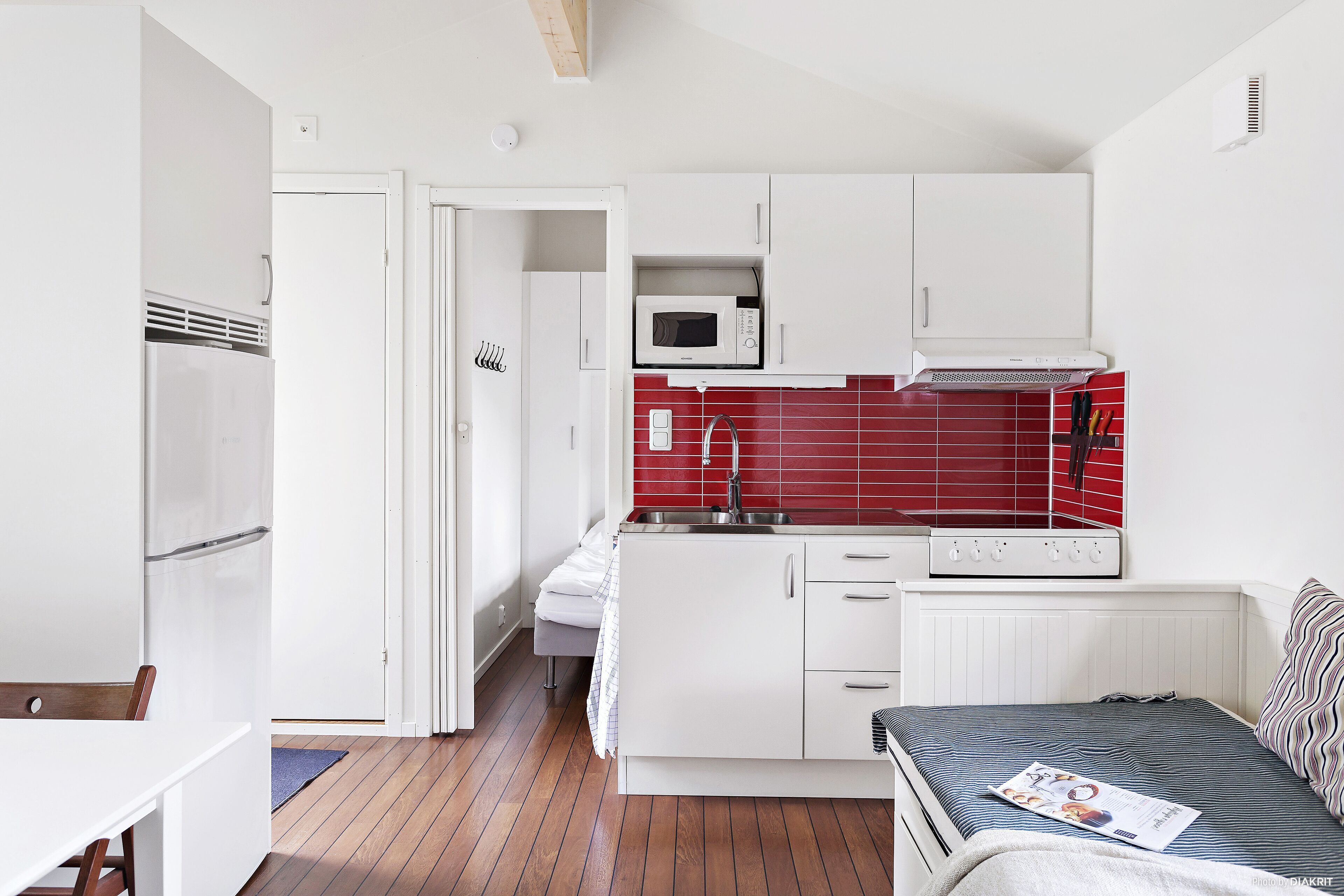 Una cocina compacta con armarios blancos, microondas y un rebozo de azulejos rojos.