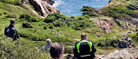 A group of people sitting on a rocky hillside overlooking a coastal landscape.