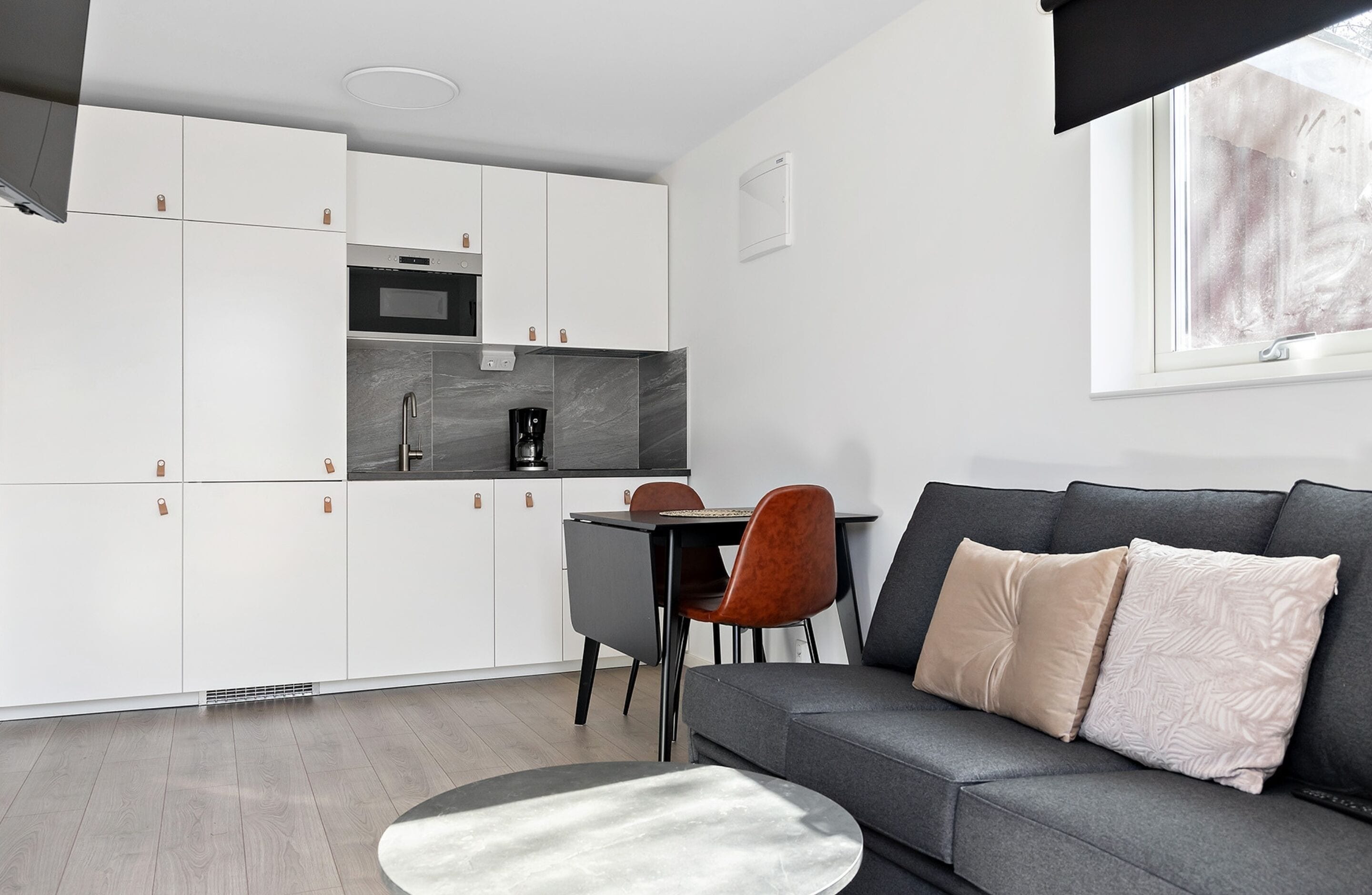 A compact living space with a kitchenette, grey sofa, and a dining area.