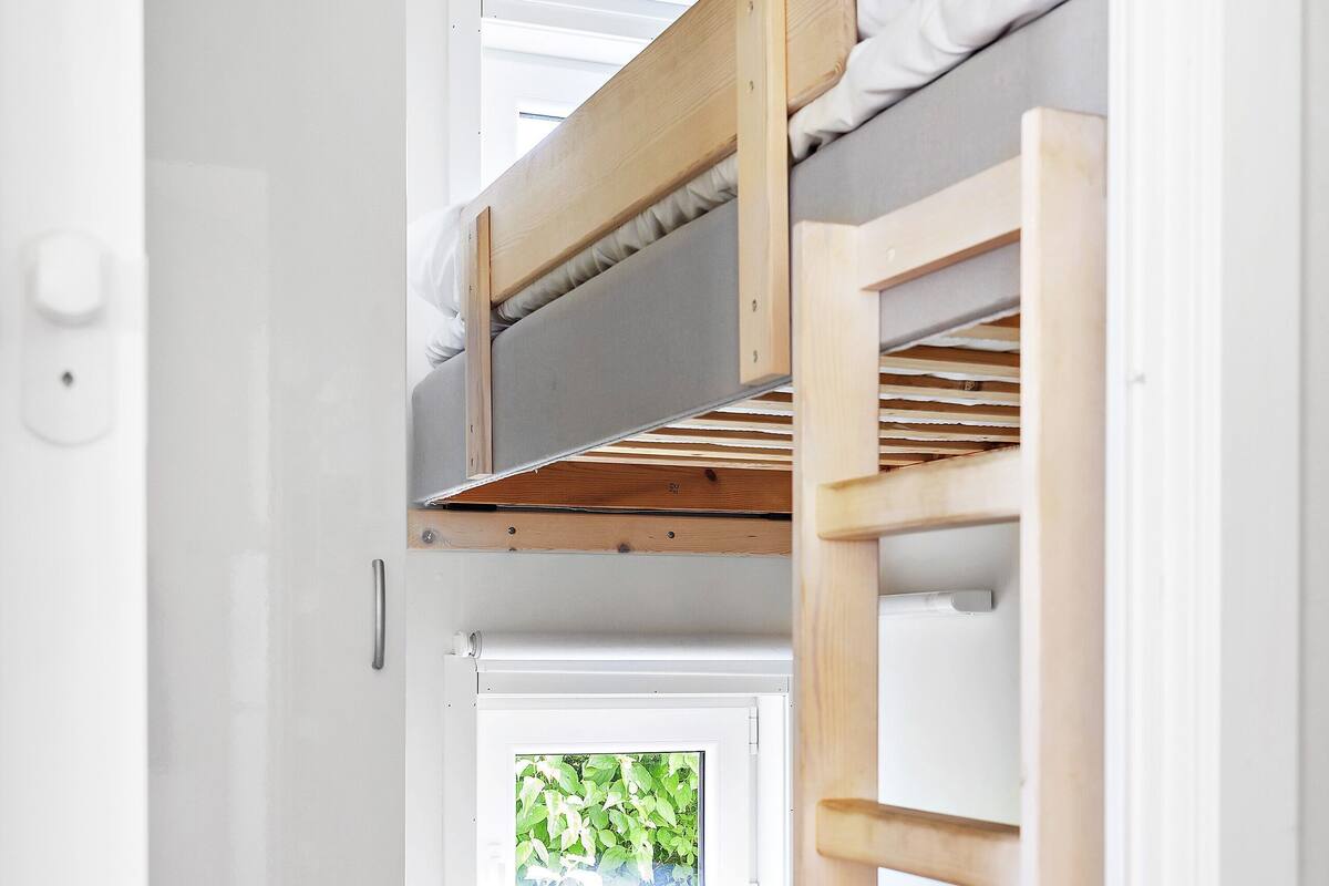 A bunk bed with a window, white walls, and a wooden floor.