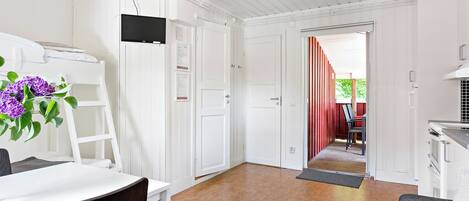 A modern interior with white walls, a dining area with a table and chairs, a kitchen area, and a hallway leading to an outdoor space.