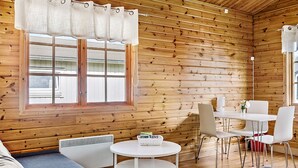 Ein Holzblockhaus-Innenraum mit Esstisch, Stühlen, einer Couch und einem Fenster mit Vorhängen.