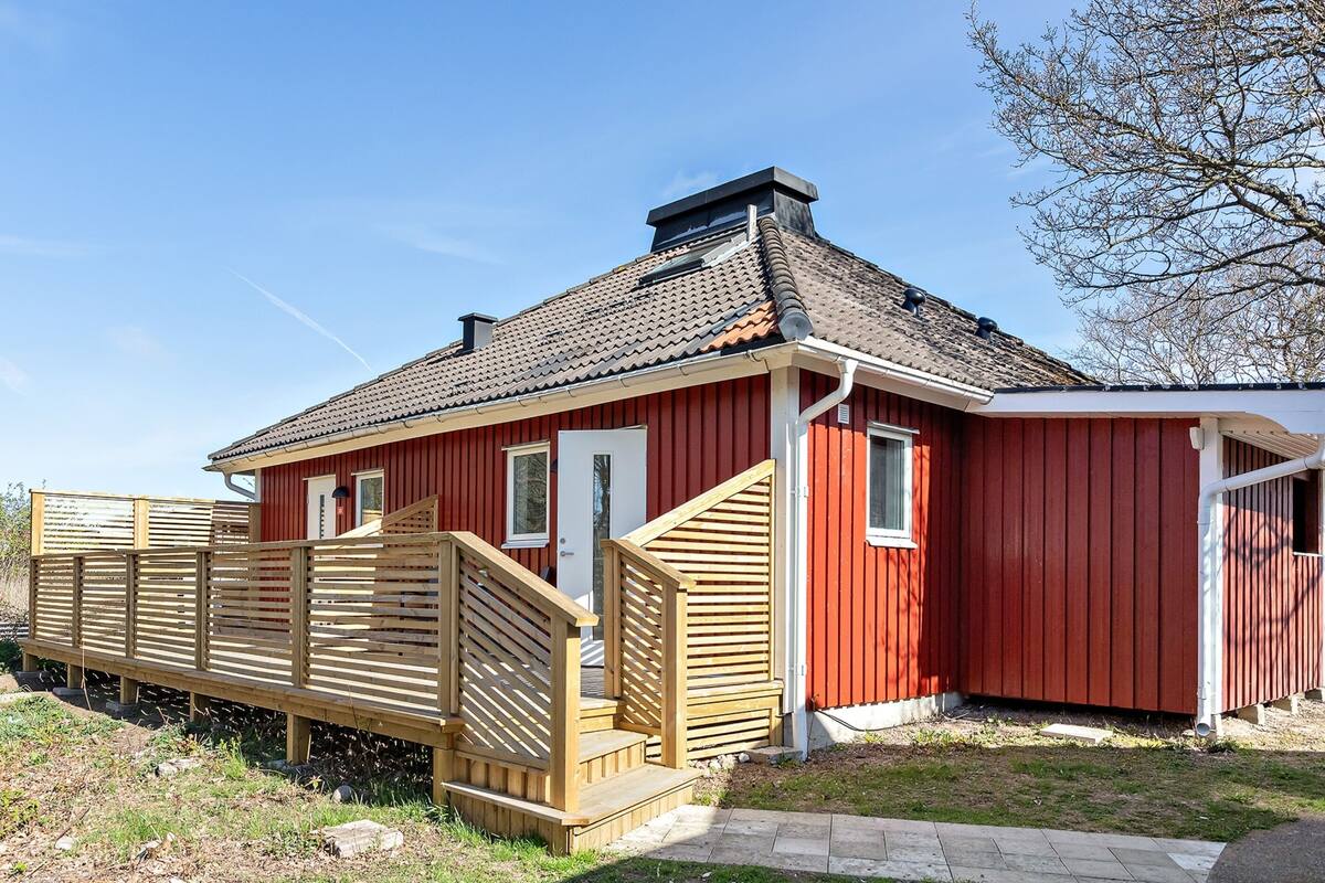 A red wooden building with a tiled roof, a wooden deck, and a small attached structure.