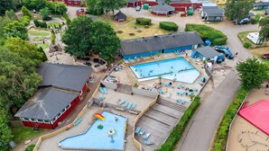 Luftaufnahme eines Resorts mit mehreren Schwimmbecken, einem Spielbereich für Kinder und verschiedenen Sitzbereichen im Freien.