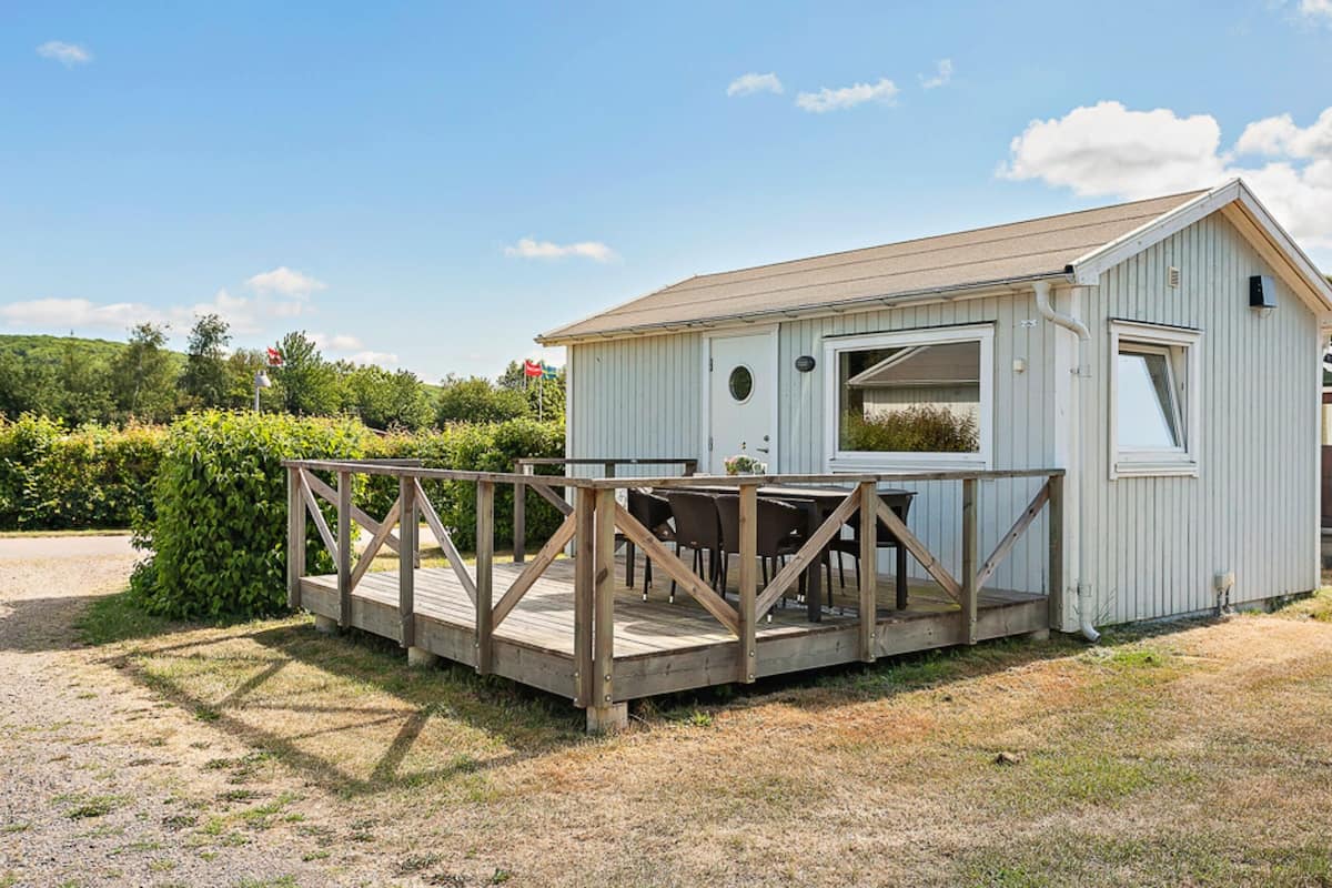 A small, single-story building with a wooden deck and a table and chairs set up outside.