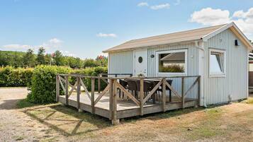 A small, single-story building with a wooden deck and a table and chairs set up outside.