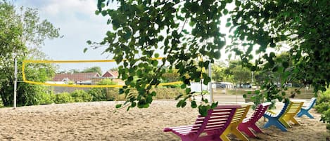 Zona de playa arenosa con sillas de playa de colores y una estructura de red amarilla.