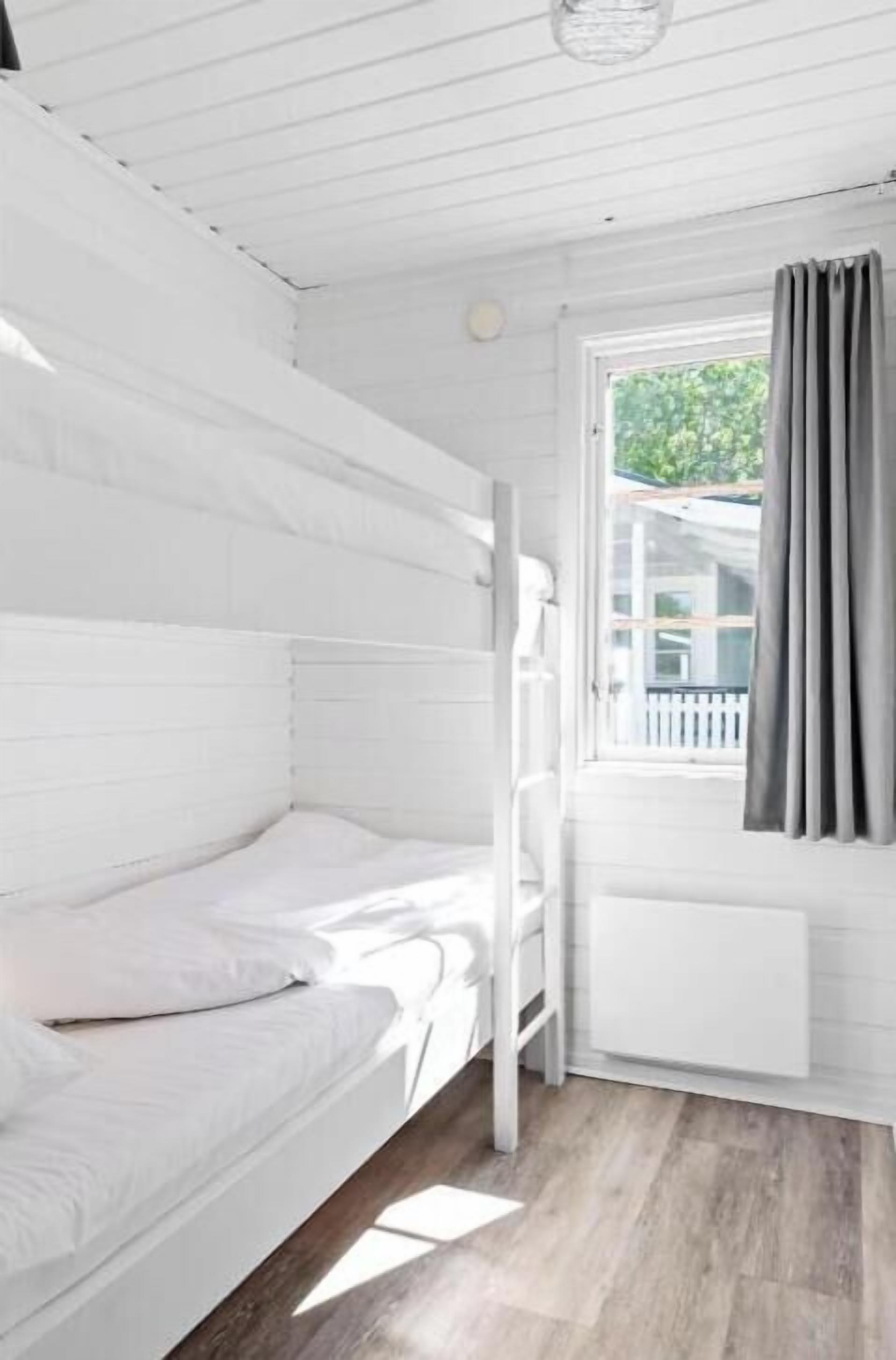 Una habitación blanca con literas, una ventana con cortinas y vistas al exterior.