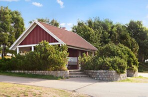 A red barn-style building with a sloped roof, surrounded by stone walls and dense greenery. - First Camp Tylösand (Halmstad)