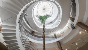 A multi-level spiral staircase with a central glass dome and a palm tree in the middle. - ALEGRIA Costa Ballena (Rota)