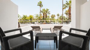 A balcony with wicker furniture and a view of palm trees and parked cars. - ALEGRIA Costa Ballena (Rota)