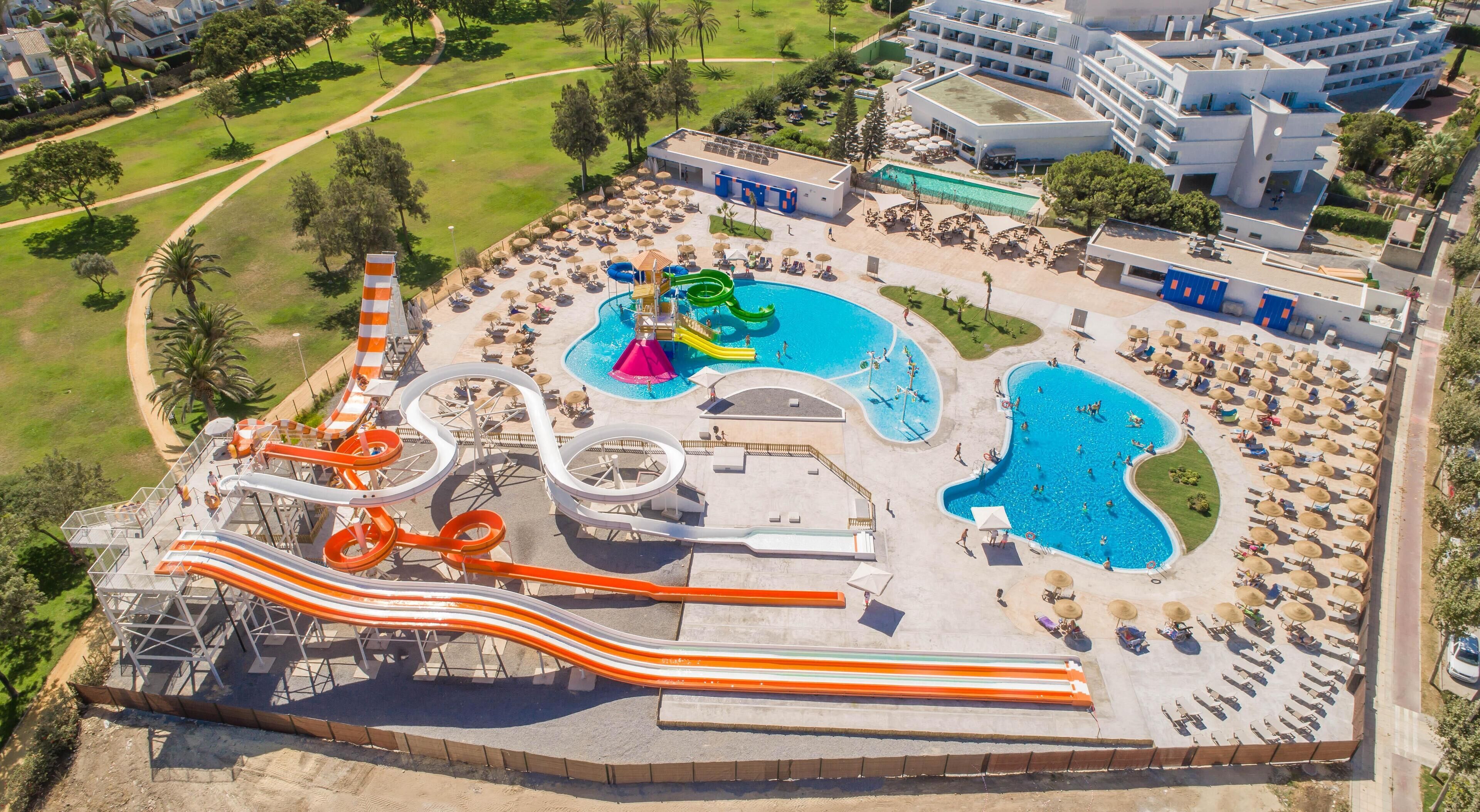 Un parc aquatique doté de nombreux toboggans et de plusieurs piscines, entouré d’un complexe hôtelier avec des chaises longues et des parasols.