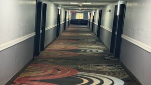 A hotel hallway with patterned carpet, doors, and a light fixture. -  Coratel Inn and Suites by Jasper Stillwater (Stillwater)