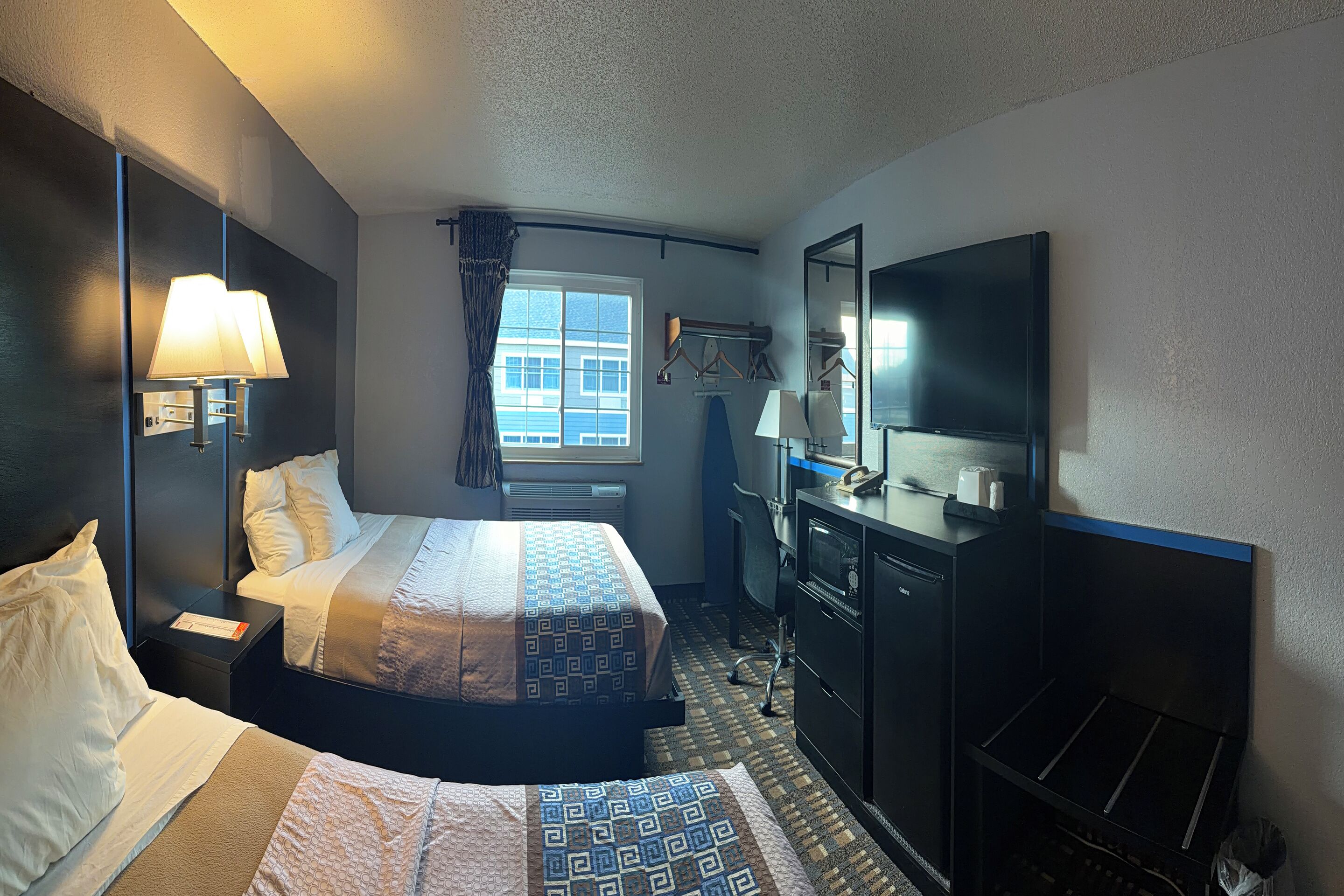 A hotel room with a bed, bedside tables, a desk, a television, and a window with curtains.