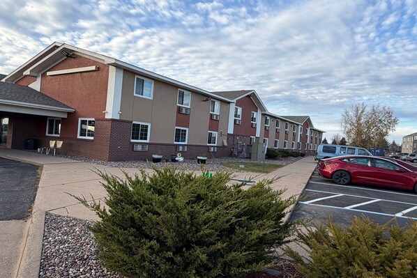 A multi-story building with a brick facade, large windows, and a parking lot with a red car. -  Coratel Inn and Suites by Jasper Stillwater (Stillwater)