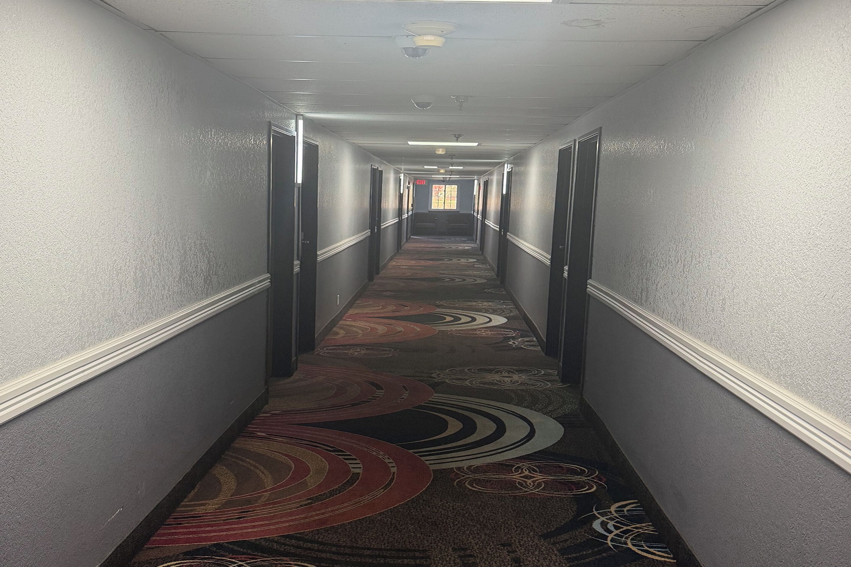 A hotel hallway with a patterned carpet, doors on both sides, and a light fixture on the ceiling.