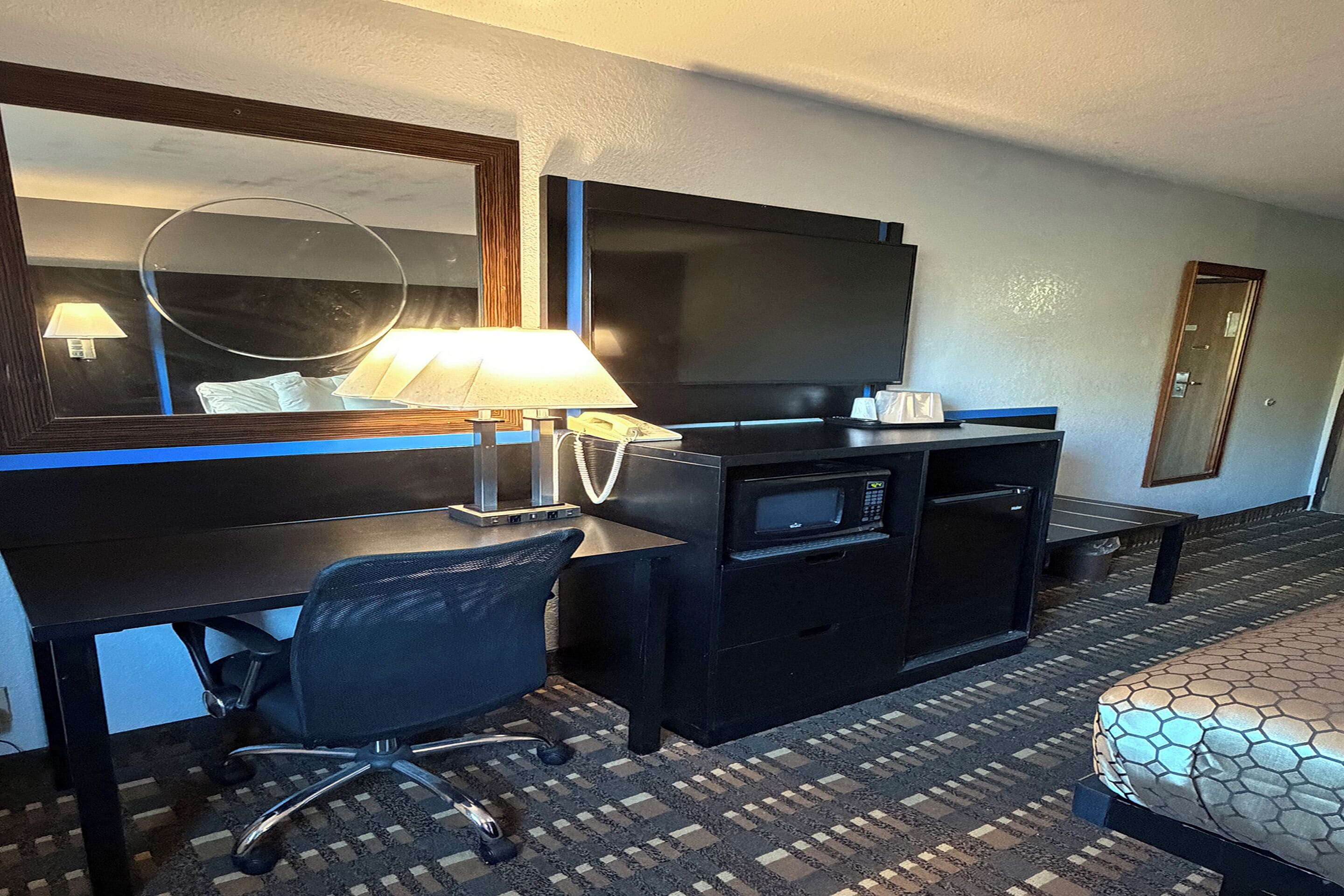 A hotel room with a desk, chair, TV, microwave, and a bed.