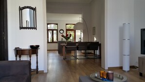 A modern living room with a wooden floor, a dining area with a table and chairs, a large mirror, and a television. - Mansion 6 (Maastricht)