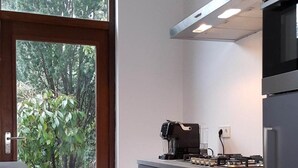 A modern kitchen with a built-in stove, a coffee maker, and a view of greenery through a large window. - Mansion 6 (Maastricht)
