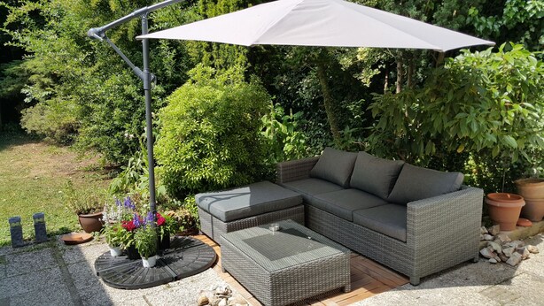 A sectional sofa with a matching ottoman and a large umbrella in a garden setting. - Mansion 6 (Maastricht)