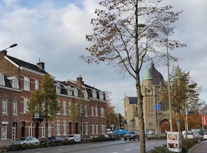 A street with traditional brick buildings, a church with a green spire, and parked cars. - Mansion 6 (Maastricht)
