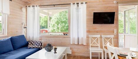 A room with wooden walls, a blue sofa, white chairs, a dining table, and a TV mounted on the wall.