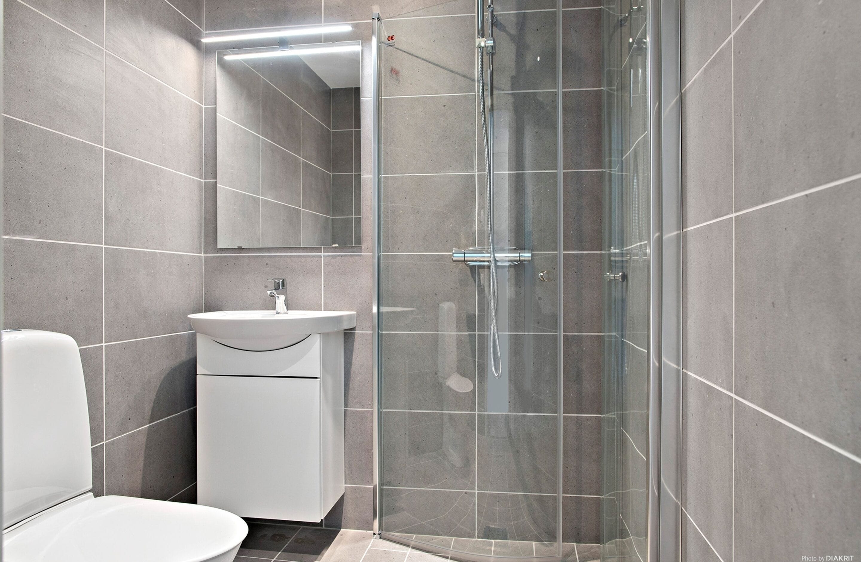 Un baño moderno con ducha envuelta en vidrio, un lavamanos blanco y un inodoro.