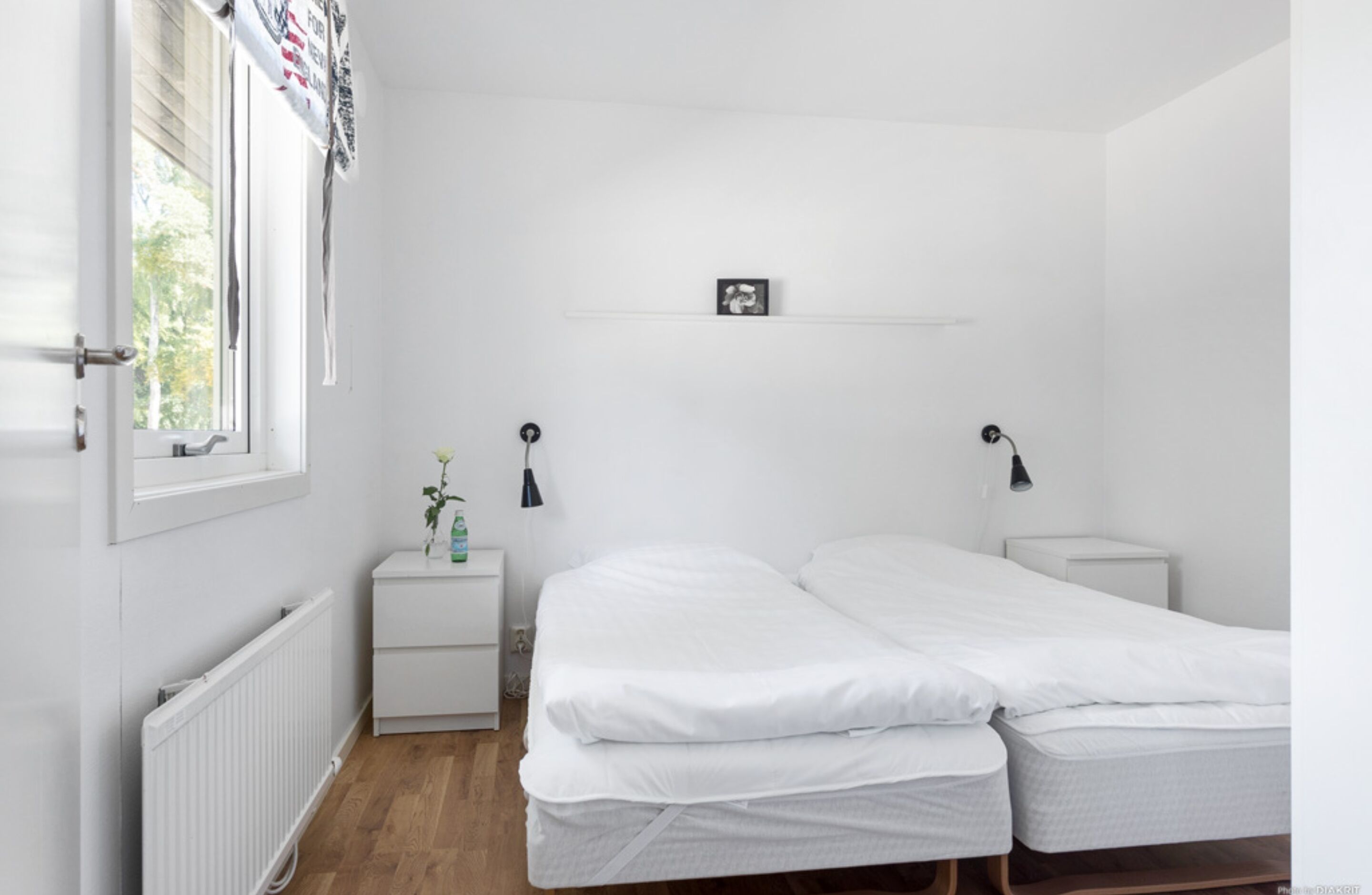 Camera da letto con due letti singoli, un comodino con lampada, un termosifone e una finestra con persiane.