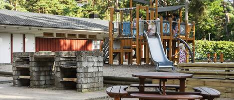 A playground with a slide, picnic tables, and a building with a red door.