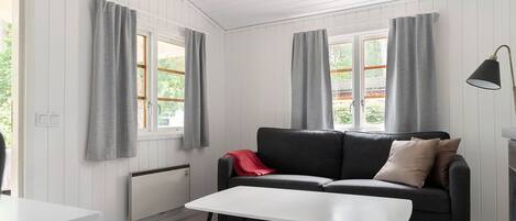 Ein modernes Wohnzimmer mit einem grauen Sofa, einem weißen Couchtisch und grauen Vorhängen an den Fenstern.