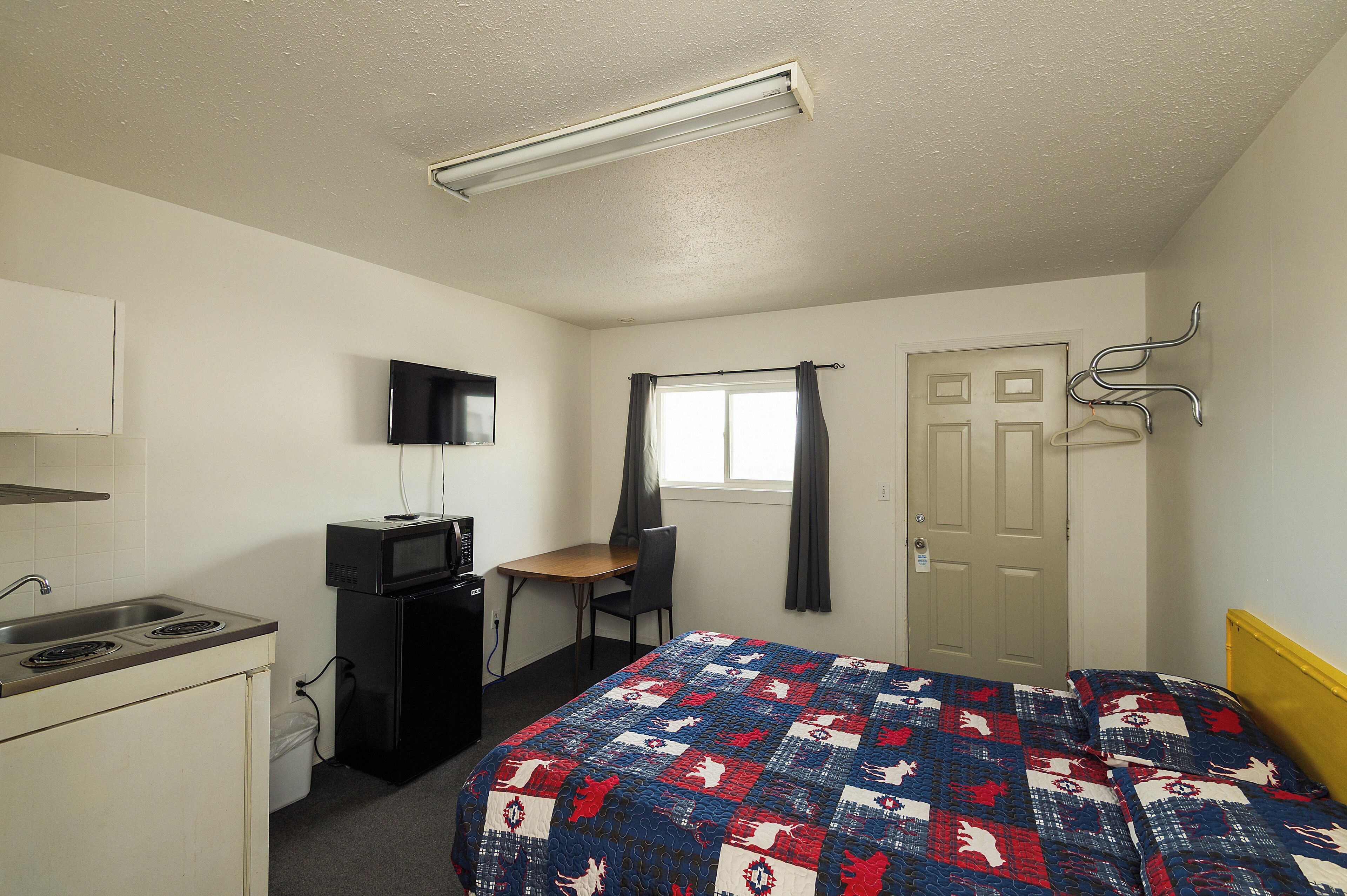 A hotel room with a bed, a desk, a TV, a microwave, and a door.