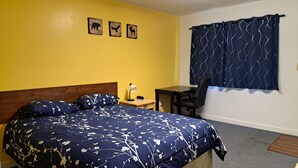 Une pièce comprenant un lit, un bureau, une chaise et une fenêtre avec des rideaux.
