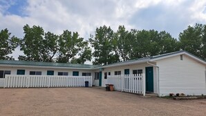 Un bâtiment blanc avec une porte verte portant l’inscription « BUREAU » et une zone délimitée par une clôture, avec des boxes numérotés.