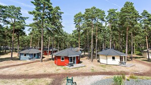 A campground with several small cabins, each with a patio and surrounded by tall pine trees.