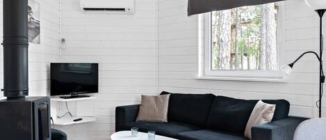 Una sala moderna con un sofá negro, una mesa de centro blanca y un televisor sobre un mueble blanco.