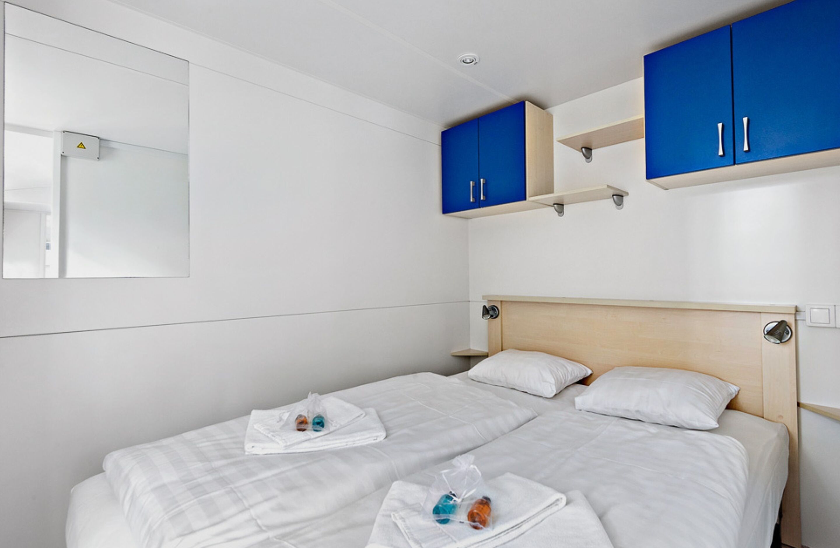Ett hotellrum med en säng, två blå skåp, en spegel och en liten hylla.