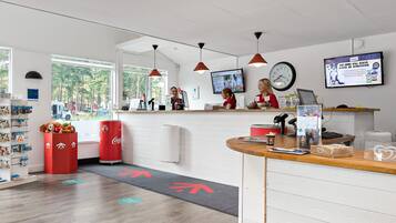 A reception area with a counter, a clock, a TV screen, and a window with a view of trees.