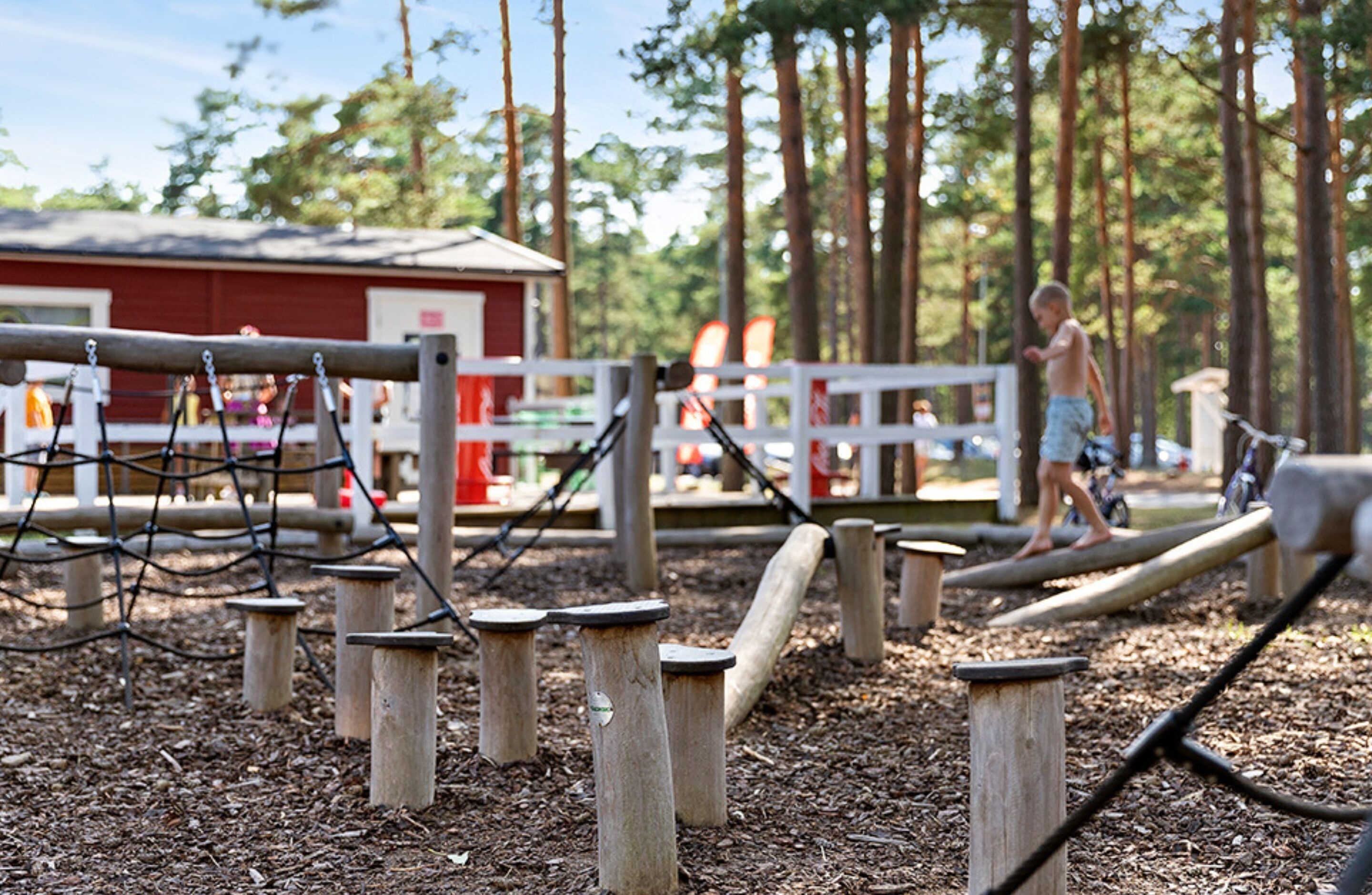 A playground with wooden structures and a red building in the background.