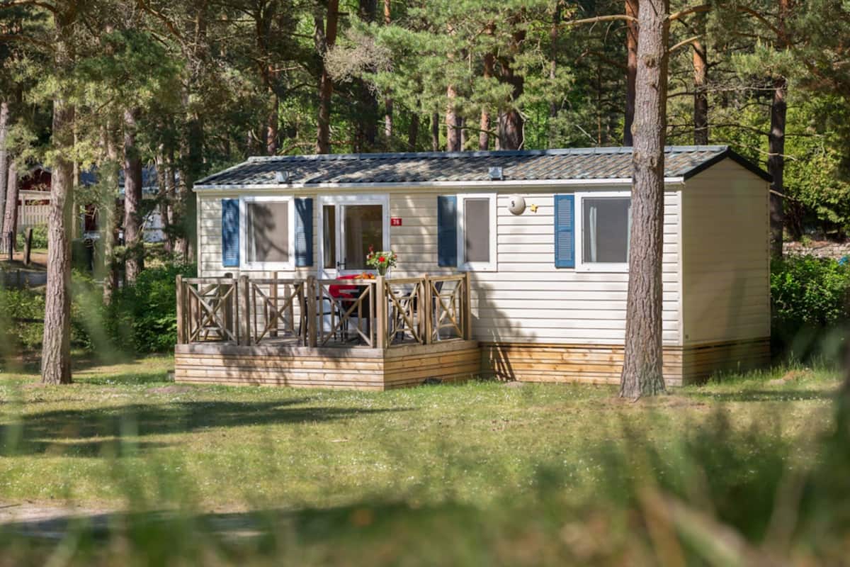 Une maison mobile dotée d’une véranda et d’une petite terrasse, entourée d’arbres.