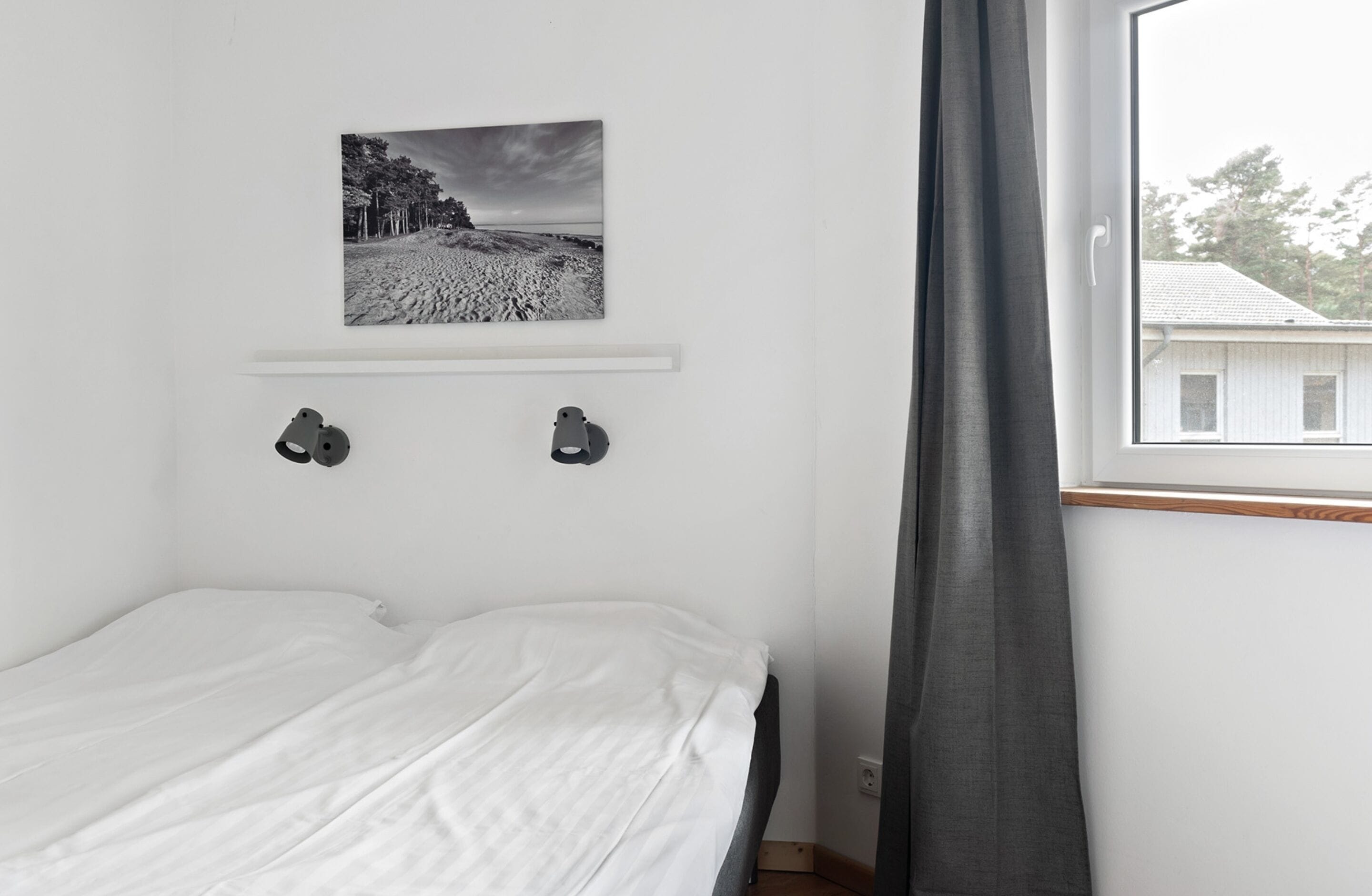 A bedroom with a bed, a picture on the wall, and a window with curtains.